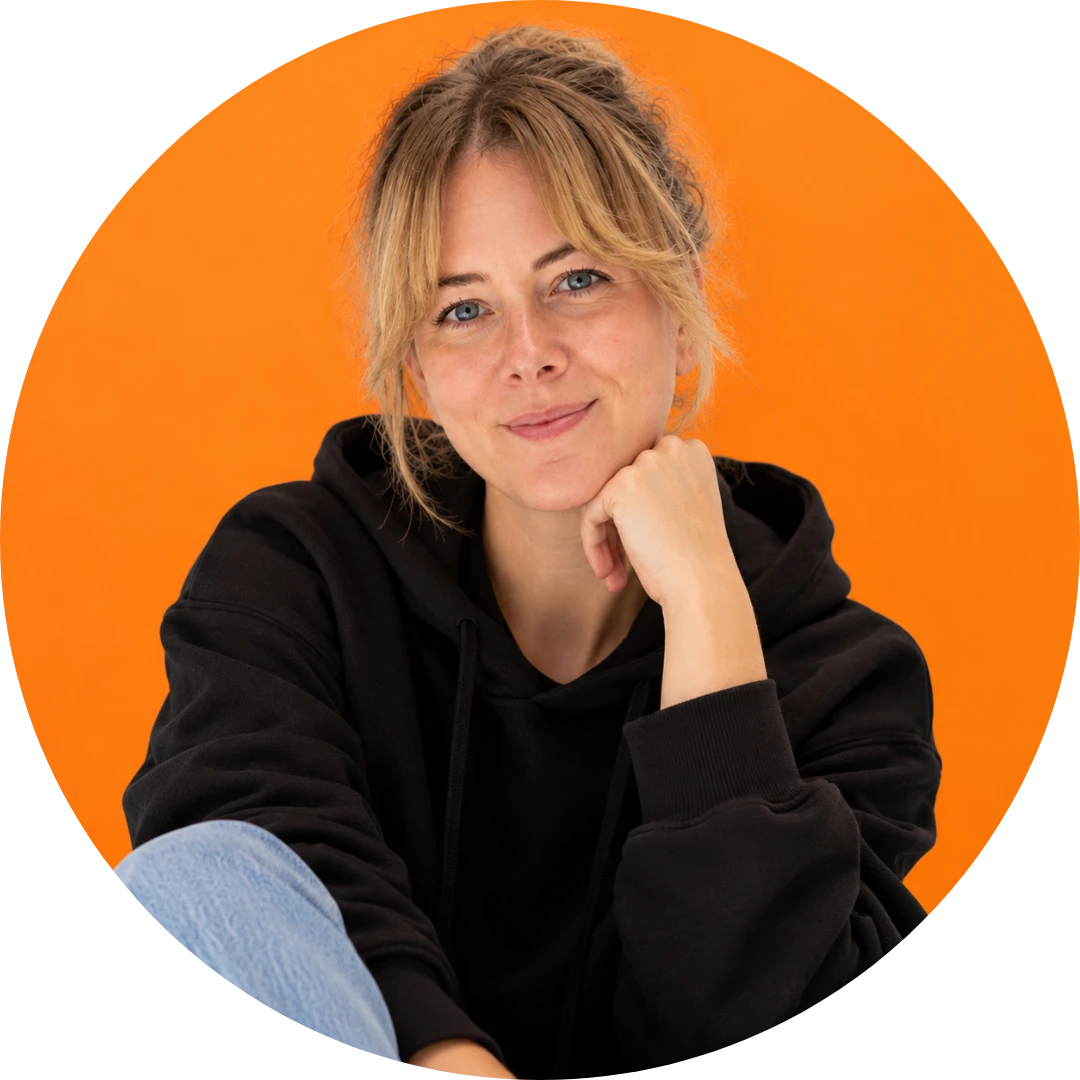 Julia Schürer, smiling, chin resting on her hand, in front of an orange background
